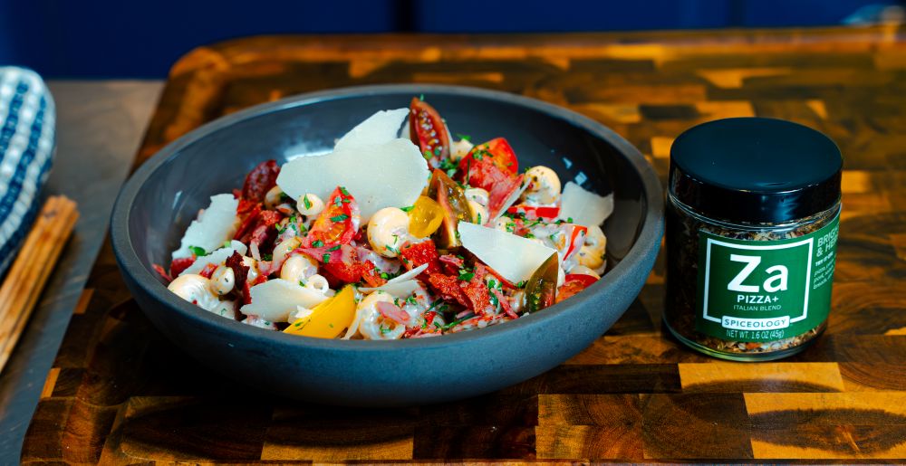 Bowl of Pepperoni Pasta Salad on a wooden cutting board next to a jar of Spiceology Pizza+ seasoning