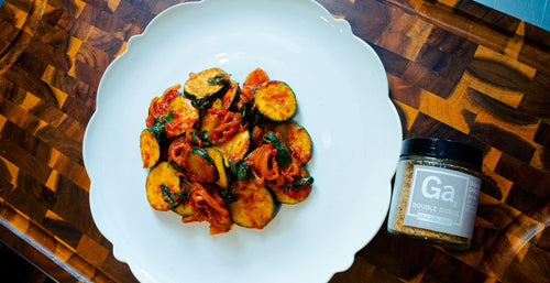 Plated Zucchini Sauté on a wood cutting board next to a jar of Spiceology Double Garlic seasoning