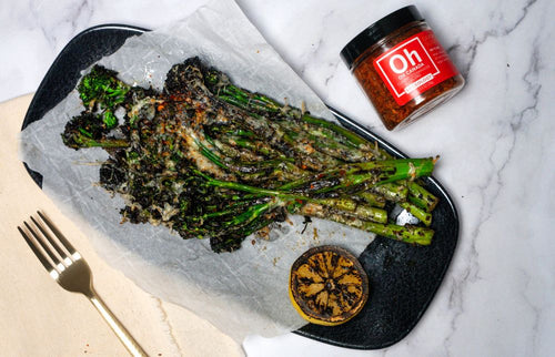 Plated charred broccolini topped with Parmesan and next to a jar of Spiceology Oh Canada seasoning