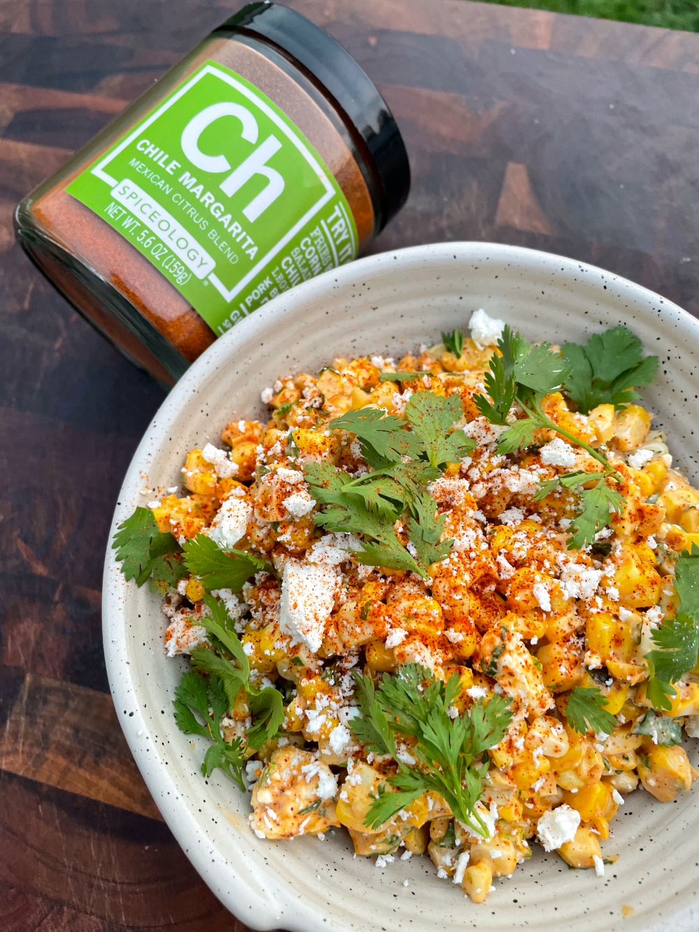 Bowl of Elote-Inspired Corn topped with cotija and cilantro Salad next to a jar of Spiceology Chile Margarita blend