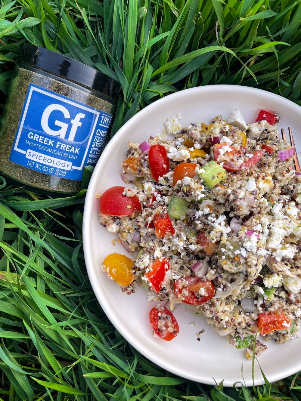 Bowl of cold Quinoa with feta and veggies next to a jar of Spiceology Greek Freak seasoning